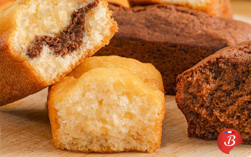 Assortiment de petits cakes moelleux Brossard, natures, marbrés et au chocolat, posés sur une planche en bois.